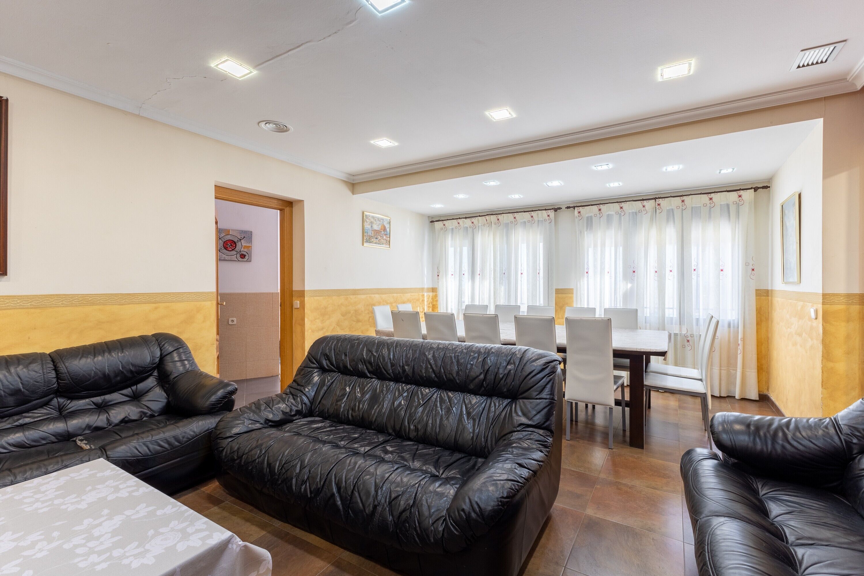 A room with two black leather sofas, a dining table with chairs, and a door leading to another room.