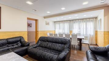 A room with two black leather sofas, a dining table with chairs, and a door leading to another room.