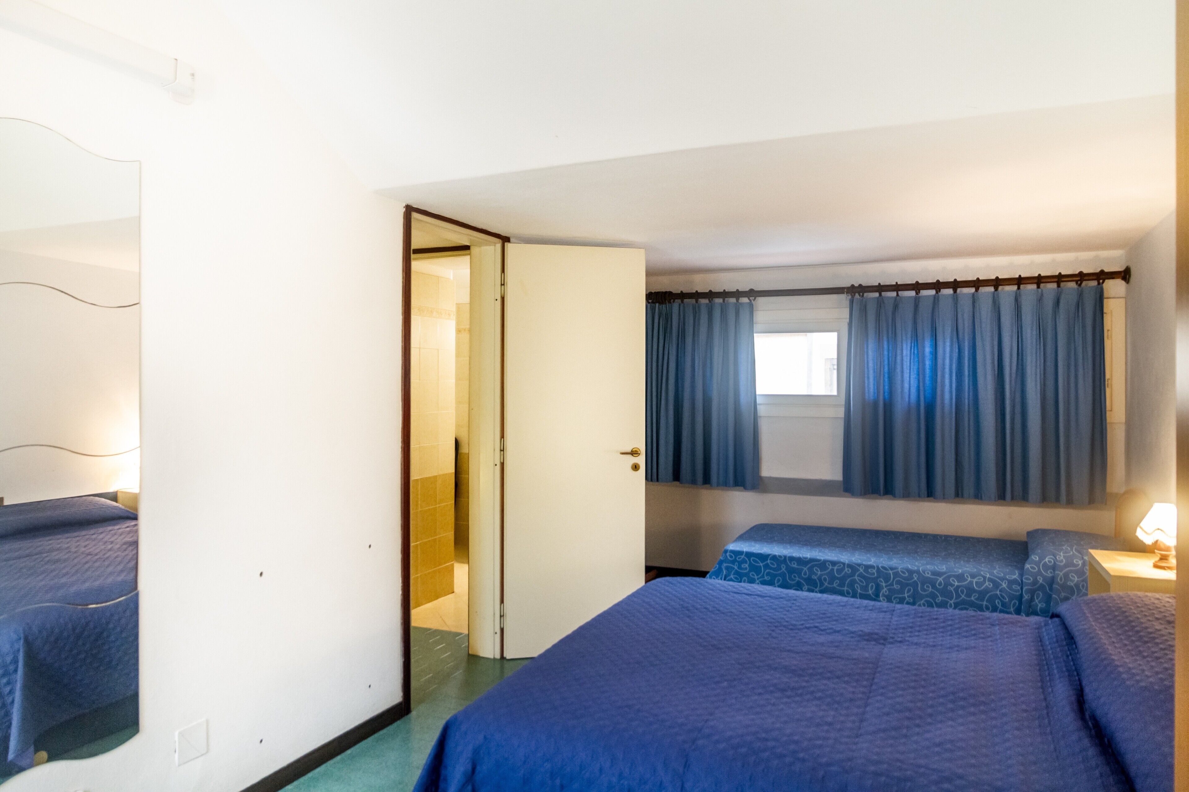Une chambre d’hôtel avec deux lits, une salle de bain et une fenêtre avec des rideaux.