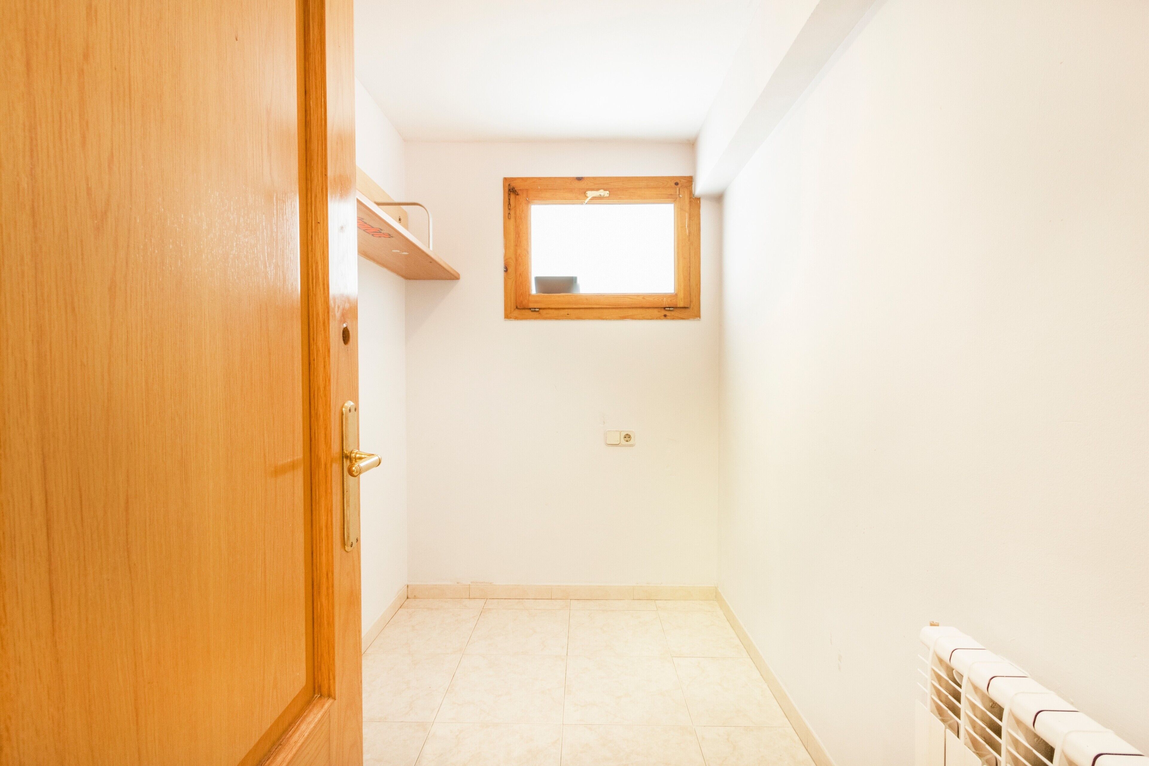 Um quarto com porta de madeira, uma pequena janela e um radiador.
