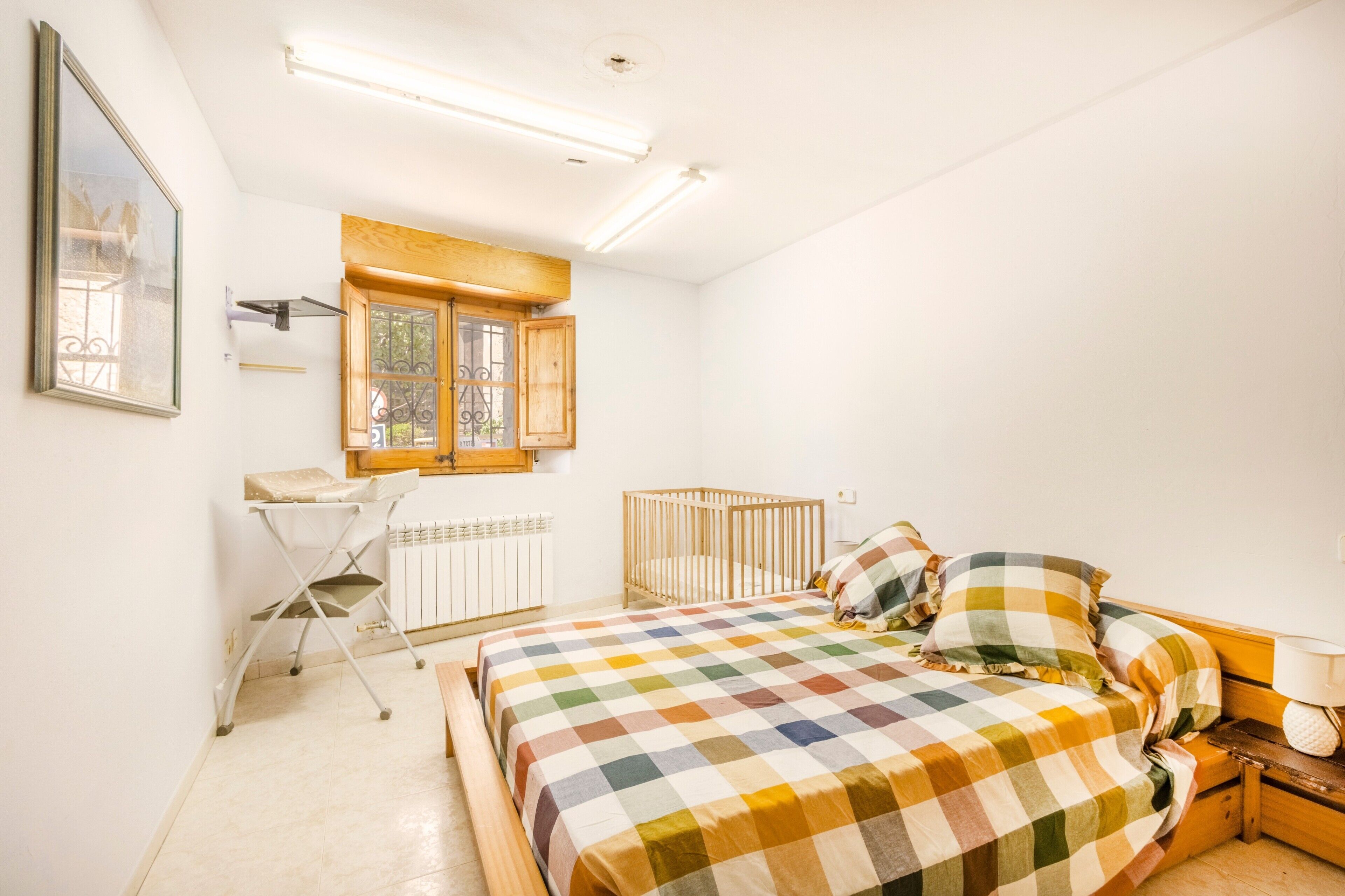 Un dormitorio con cama, cuna, ventana, radiador y escritorio con silla.
