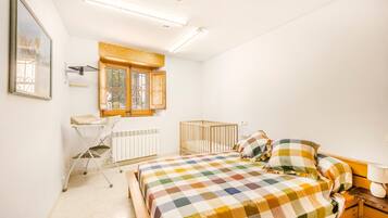 Un dormitorio con cama, cuna, ventana, radiador y escritorio con silla.