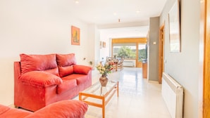 A spacious living room with a red sofa, a glass coffee table, and a view through an open door to a dining area. - Apartment 'Cal Confianza' with Mountain View, Private Garden and Wi-Fi (Borredà)