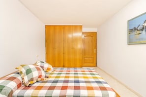 Quarto com colcha xadrez, guarda-roupa de madeira e um quadro na parede.