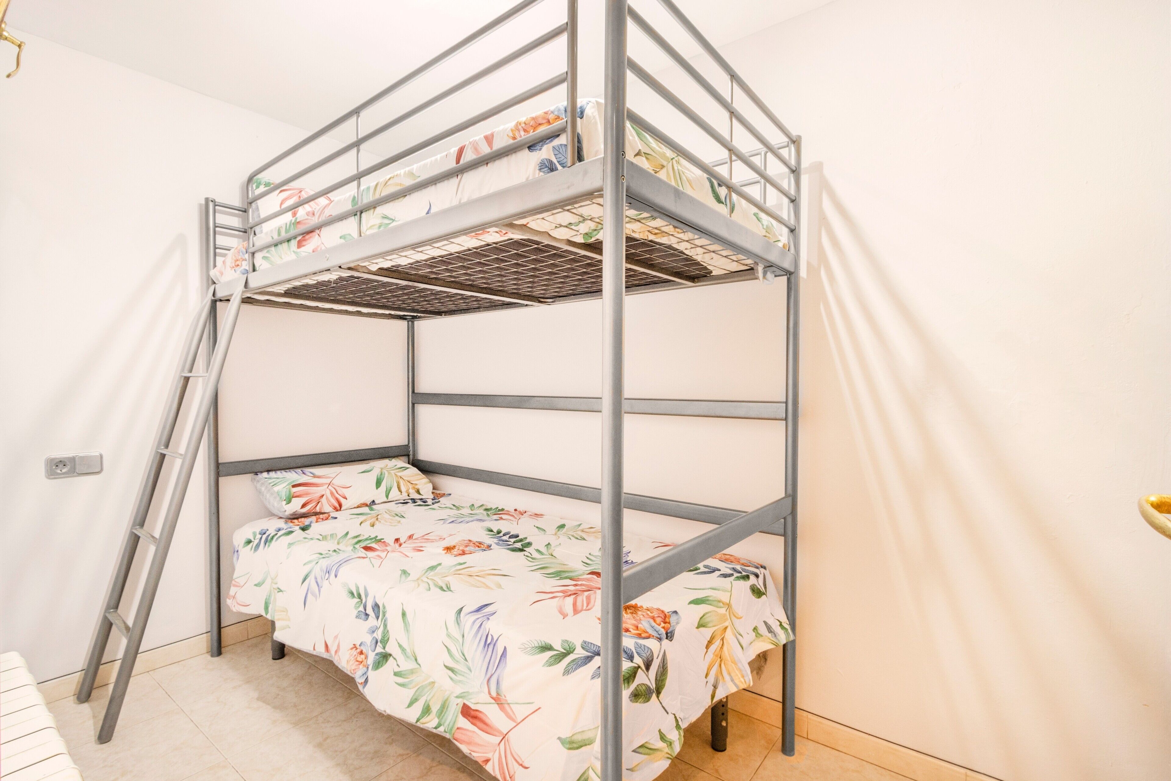 Una cama litera con colcha de estampado floral, una escalera y una pared lisa.