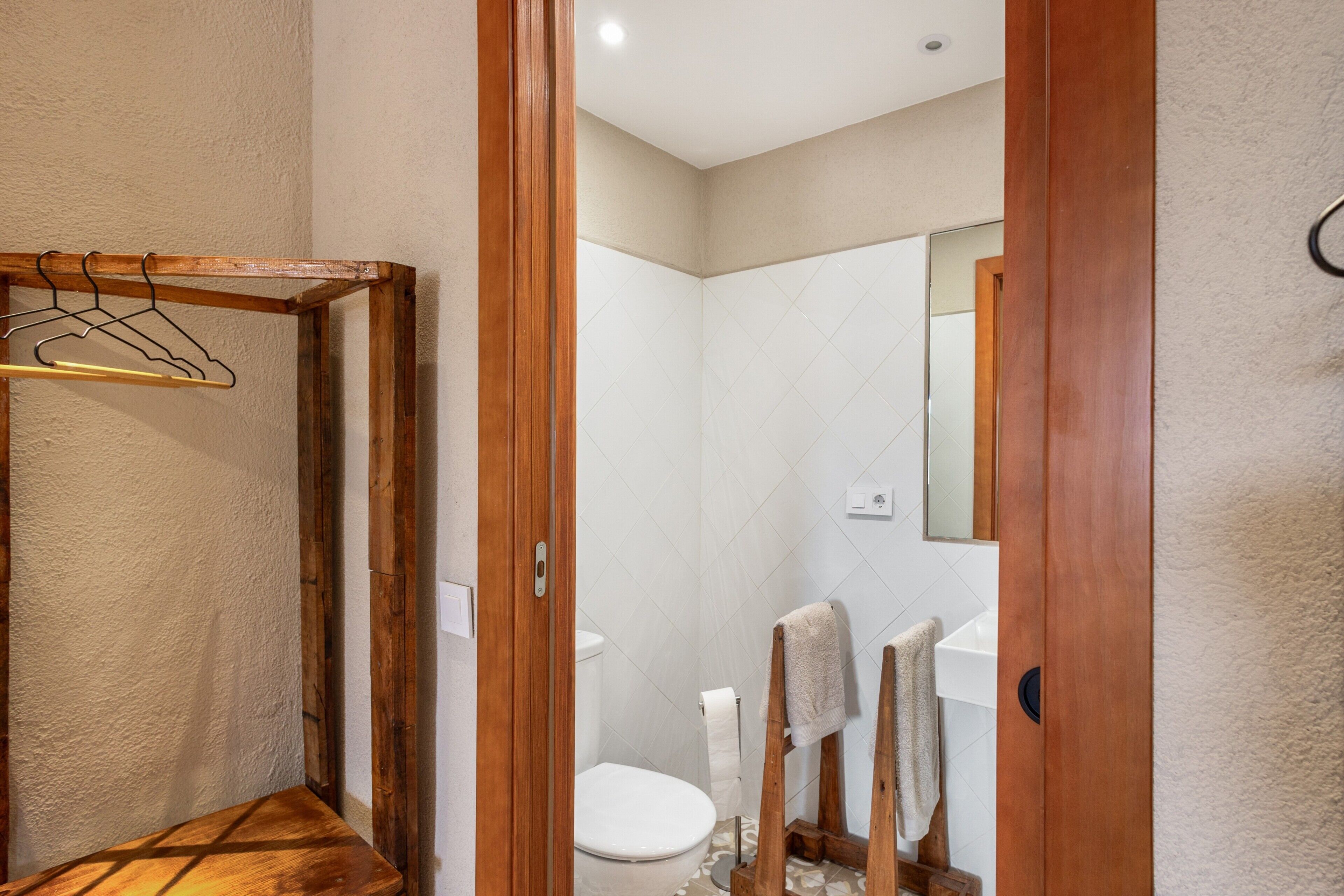 Un baño con un banco de madera, un perchero, un inodoro y un espejo.