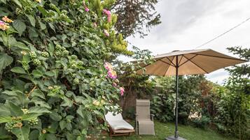 Jardín con una silla de descanso y sombrilla, rodeado de follaje y plantas florecientes.