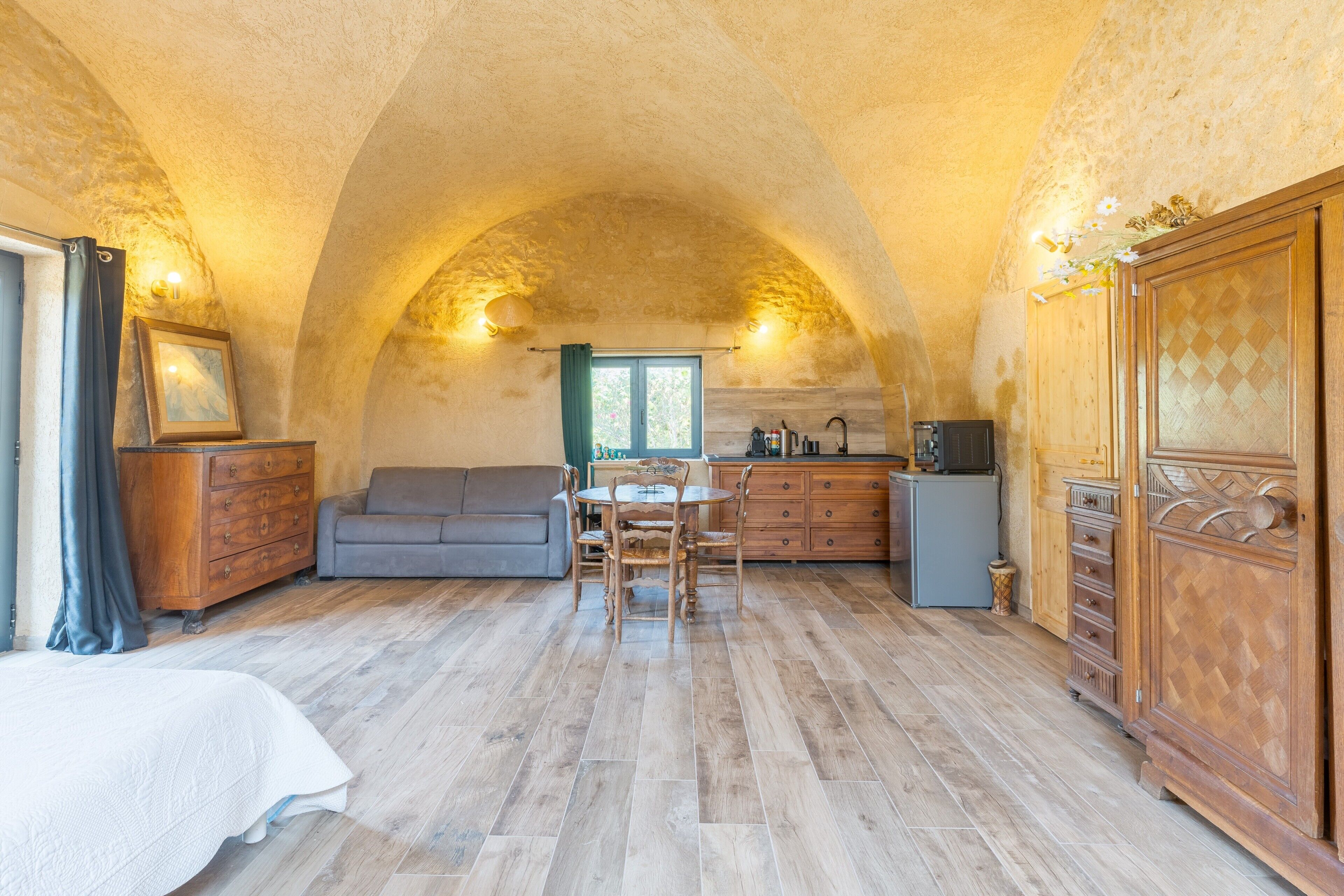 Una habitació acollidora amb un sostre voltaic, una taula de dinar amb cadires, un sofà, un armari i un llit.