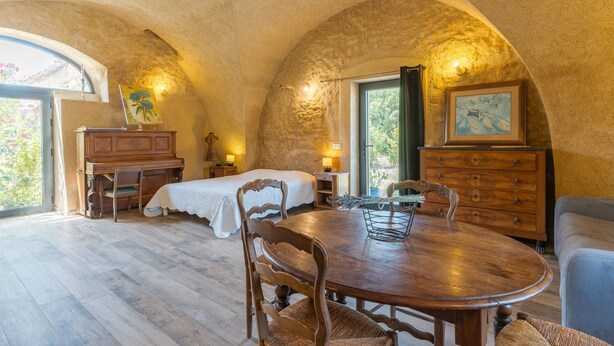 A rustic room with a wooden dining table, two beds, and a large window. - Studio Apartment 'L'Amaryflor' with Private Garden (Vaugines)