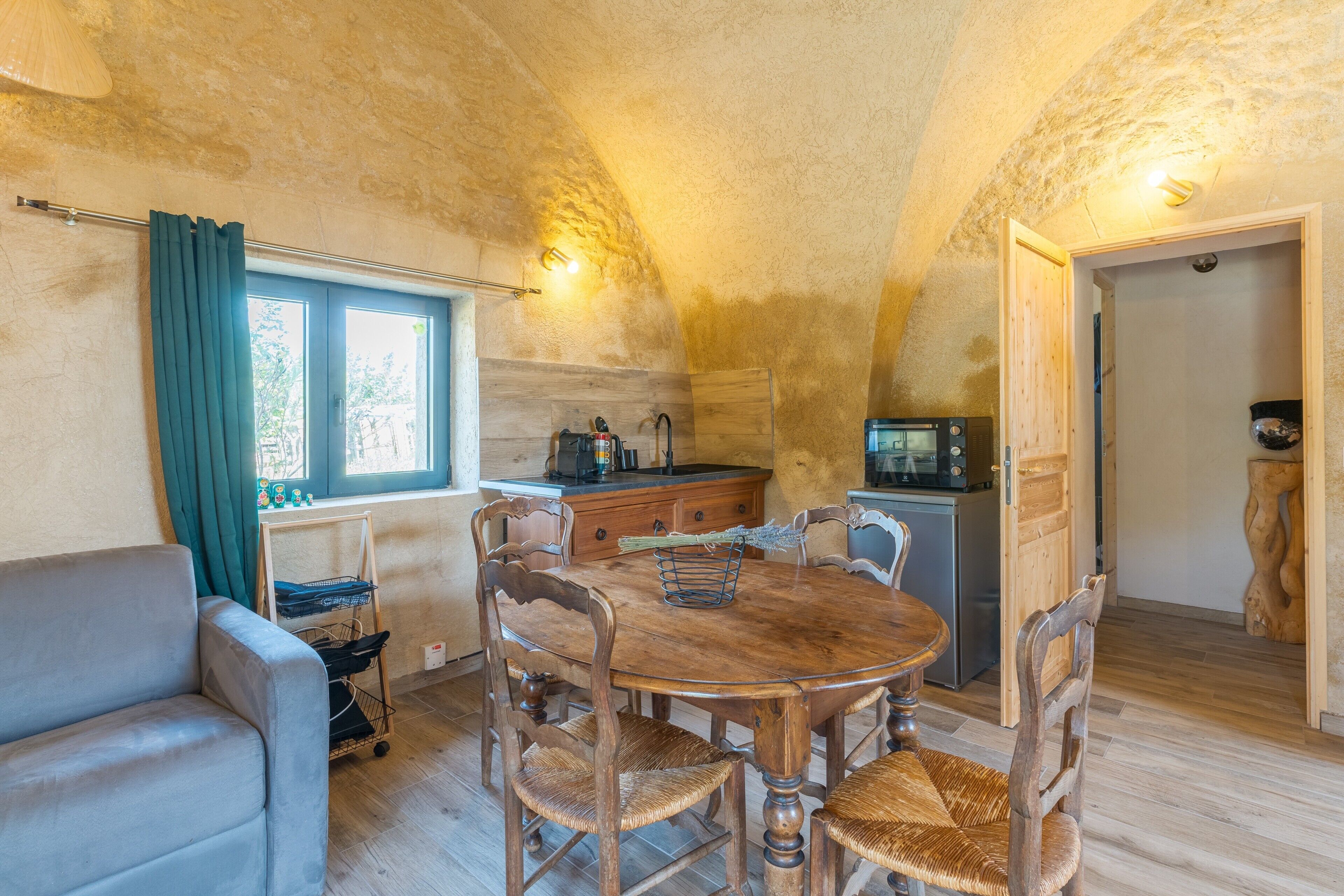 A cozy dining area with a wooden table and chairs, a sofa, and a kitchen area with a microwave and cabinets.