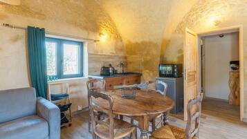 A cozy dining area with a wooden table and chairs, a sofa, and a kitchen area with a microwave and cabinets.