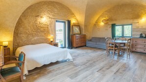 A bedroom with a bed, a wooden dresser, a dining table with chairs, and a sofa. - Studio Apartment 'L'Amaryflor' with Private Garden (Vaugines)
