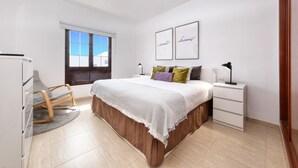 Une chambre à coucher avec un lit, des tables de chevet, une chaise, une fenêtre et des tableaux encadrés au mur.