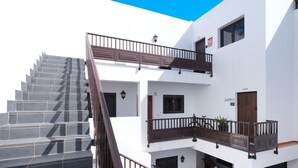 Un immeuble à plusieurs étages, avec un escalier menant à un balcon, une porte portant un numéro et une petite plante au rez-de-chaussée.