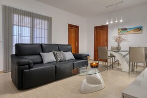 Un salon moderne avec un canapé en cuir noir, une table basse en verre et un coin repas comprenant une table et des chaises blanches.
