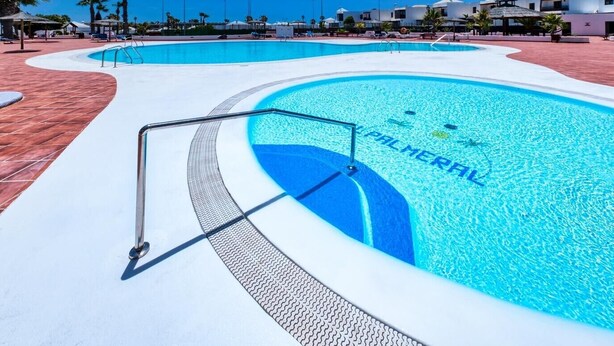 Une piscine, avec un ciel bleu dégagé et des palmiers en arrière-plan.