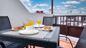 Un balcon avec une table préparée pour le petit-déjeuner, comprenant des croissants, du jus de fruits et du café.