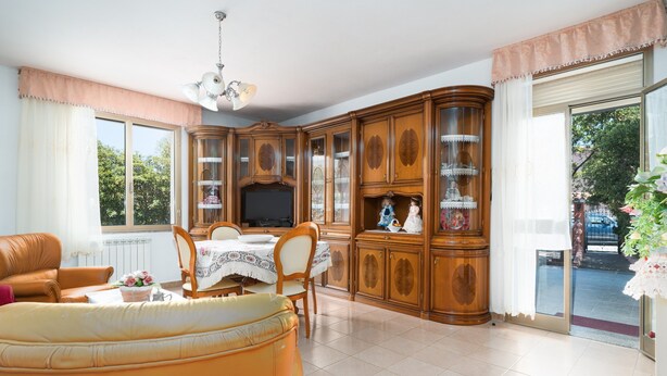Een woonkamer met een bank, een eettafel met stoelen, een televisie en houten kasten met glazen deuren.