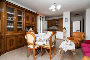 A dining area with wooden cabinets, a table with a floral tablecloth, and a leather armchair. - Holiday Home 'Casa Monica' with Shared Terrace and Shared Garden (Posada)