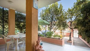 Een overdekt terras met een tafel, stoelen, een beeld en een groene parasol.