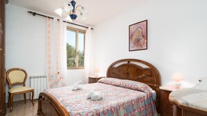 Een slaapkamer met een houten bed, een stoel, een nachtkastje met een lamp en een raam met gordijnen.