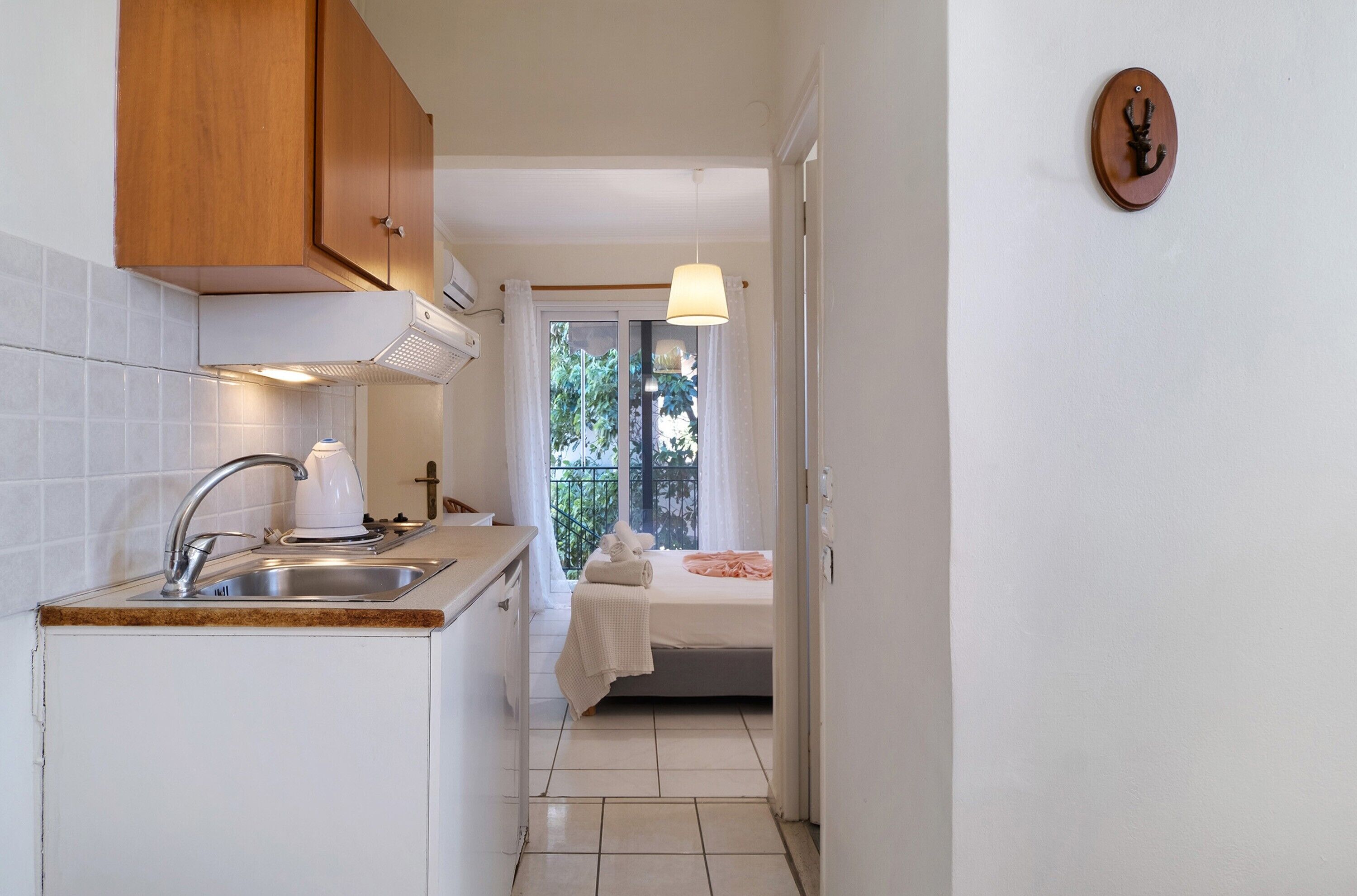 A compact kitchen with a sink, stove, and wooden cabinets, leading to a balcony with a bed and a hanging light.