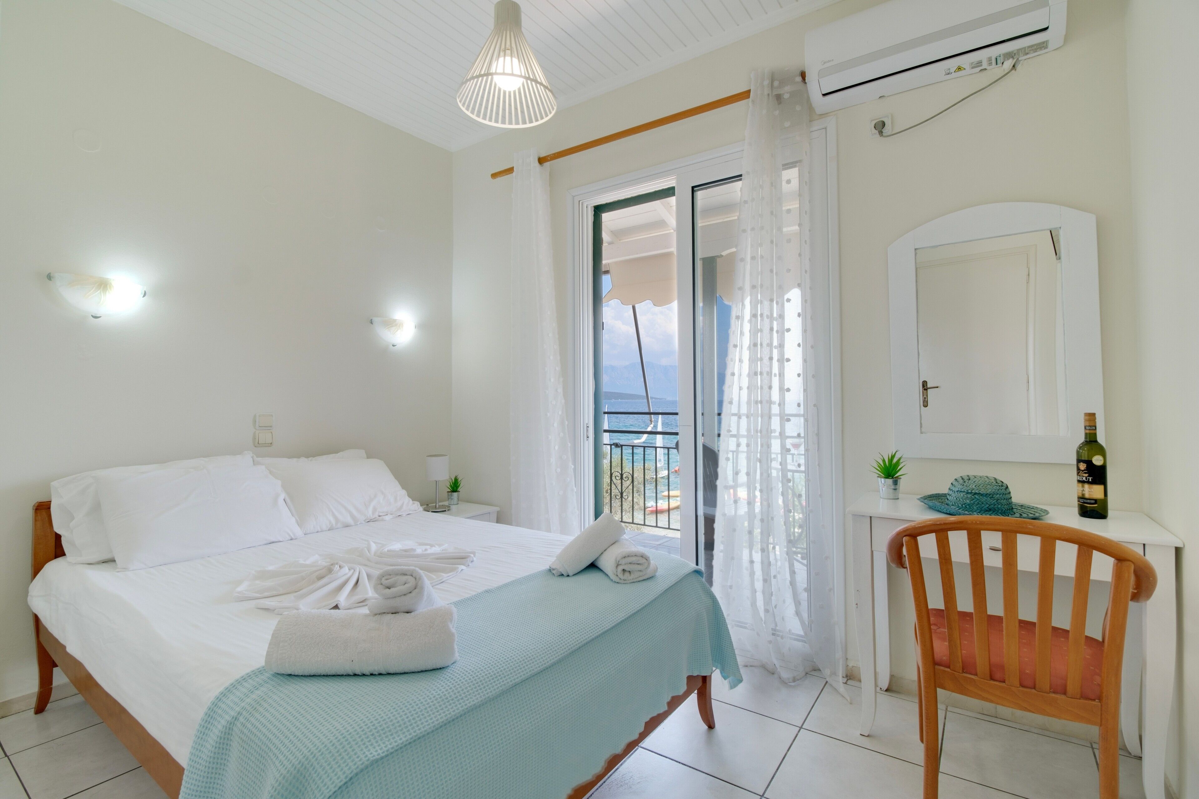 Un dormitorio con cama, una silla, escritorio, espejo y vistas al exterior.