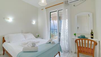 Un dormitorio con cama, una silla, escritorio, espejo y vistas al exterior.