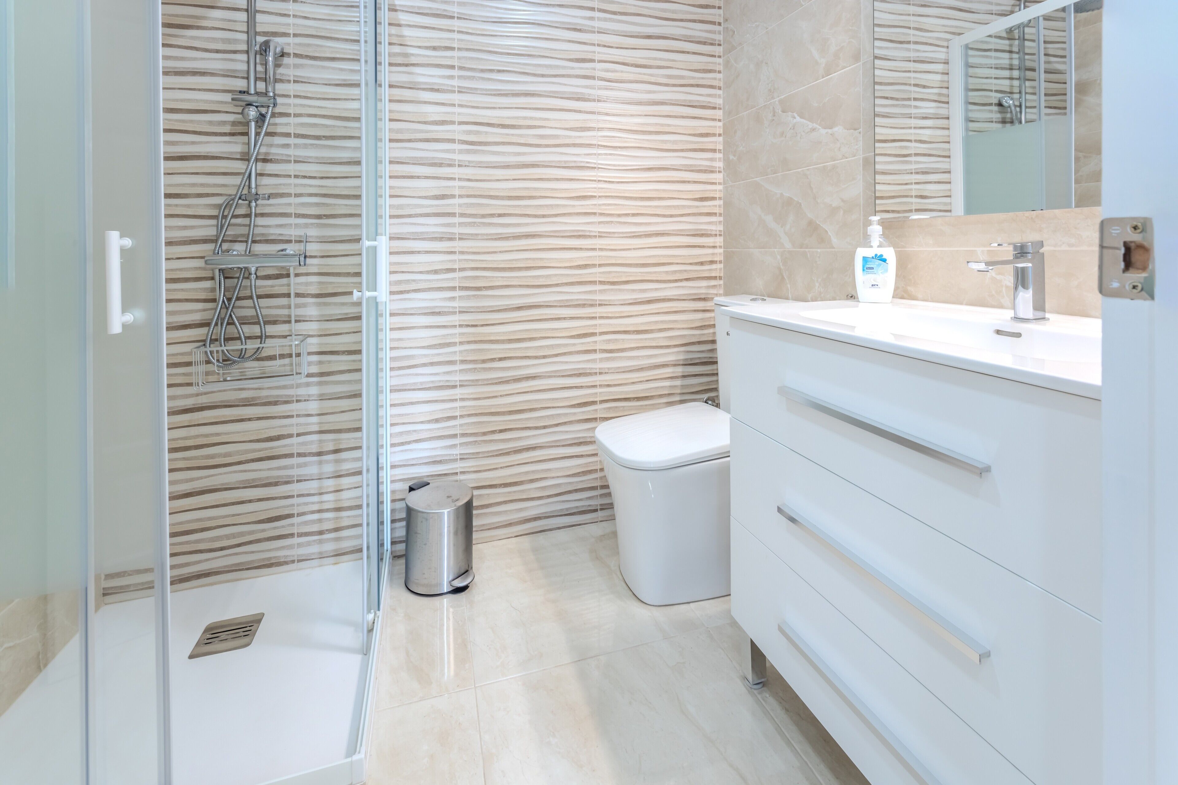 A modern bathroom with a glass-enclosed shower, a white vanity with drawers, a toilet, and a wall-mounted mirror.