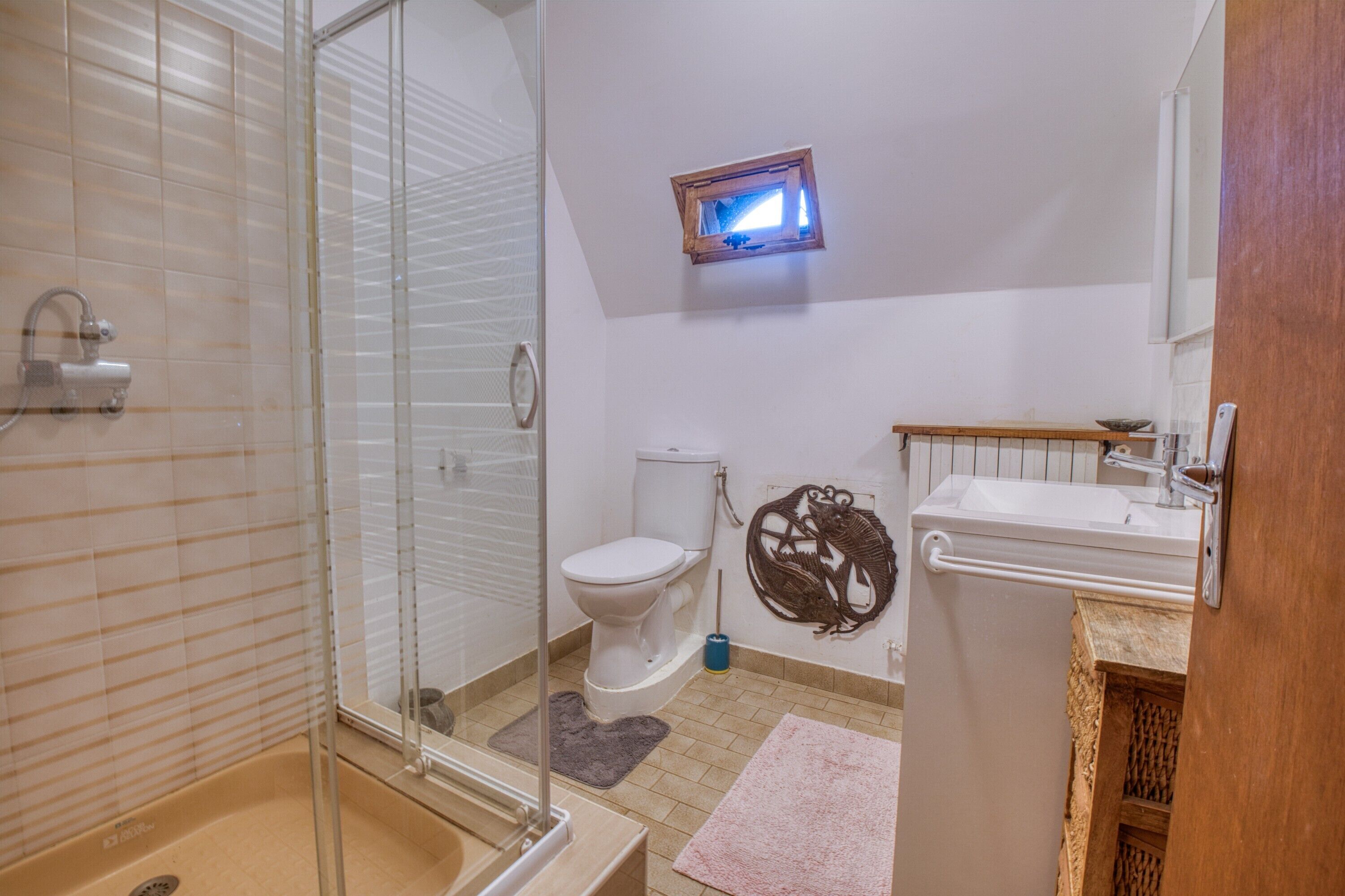 A bathroom with a glass shower enclosure, a toilet, a sink, and a small window.