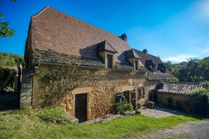 Un bâtiment en pierre avec un toit en pente, une porte en bois et un petit jardin.