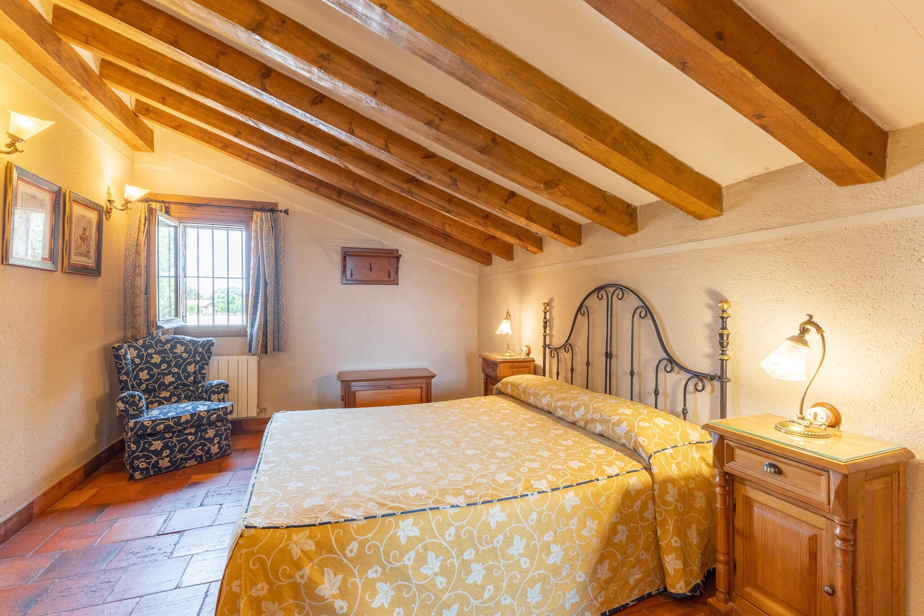 Une chambre à coucher avec un lit, une chaise, une table de chevet et une fenêtre avec des rideaux.