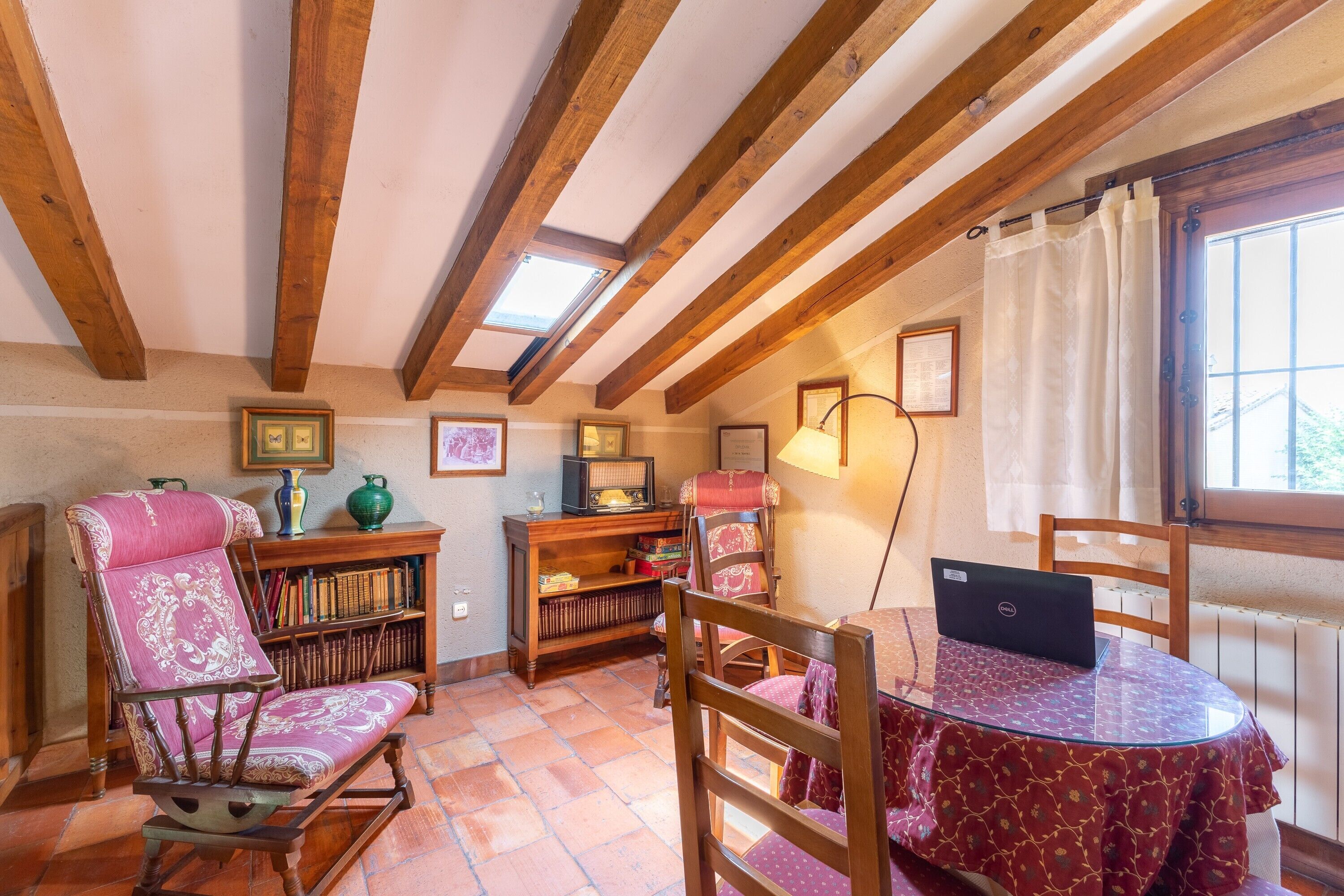Une pièce chaleureuse avec un plafond en bois, un fauteuil à bascule, une table avec un ordinateur portable et une bibliothèque.