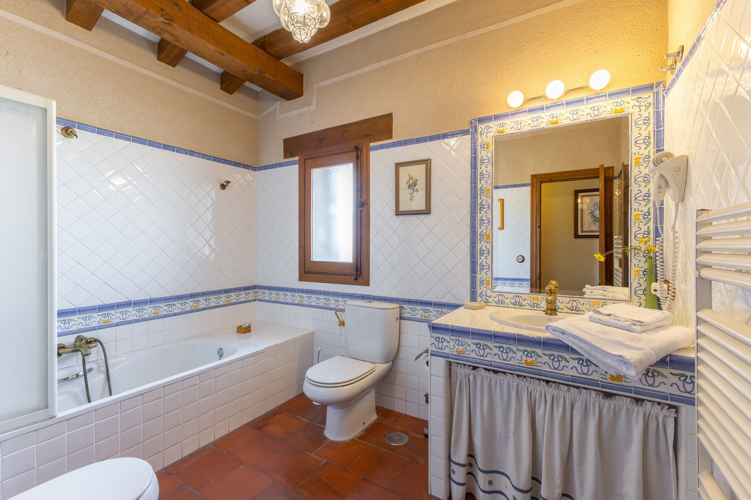 Bagno con vasca, toilette e lavandino, caratterizzato da piastrelle blu e bianche e un trave in legno al soffitto.