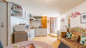 A compact kitchen with white cabinets, a microwave, and a wooden cabinet. There is a dining table with a patterned tablecloth and a jar of jam. - Apartment 'Les Cerisiers' with Shared Pool, Shared Terrace and Wi-Fi (Apt)