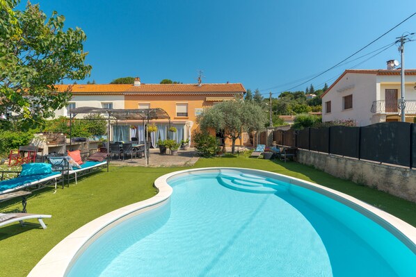 A swimming pool with lounge chairs, a patio area, and a house in the background.