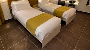 A hotel room with two beds, a bedside table, a chair, a desk, and a window with blinds. - 'Joyfül Accomodation Camera 1' with Wi-Fi and Air Conditioning (Finale Ligure)