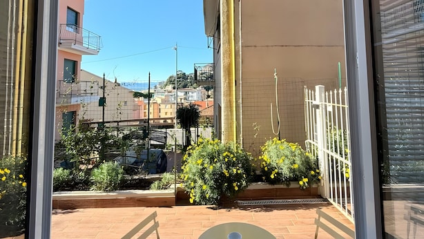 A view through a window with a metal frame, a white table, and yellow flowers in the foreground. - 'Joyfül Accomodation Camera 1' with Wi-Fi and Air Conditioning (Finale Ligure)