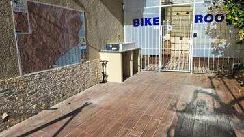 Une entrée d’immeuble avec une carte affichée sur le mur, un support à vélos et un portail portant l’inscription « LOCAL À VÉLOS ».