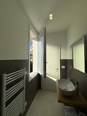 Une salle de bain moderne avec une grande fenêtre, un lavabo blanc et un porte-serviettes.