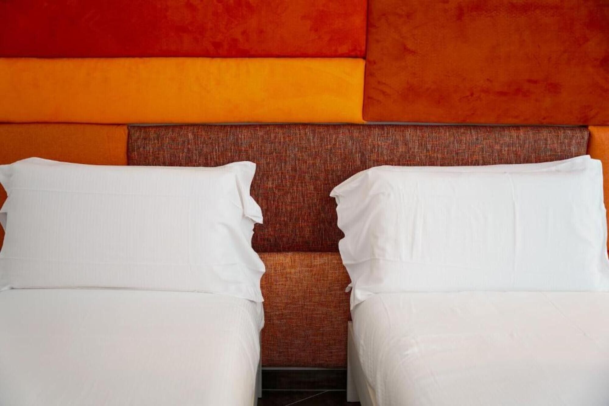 A hotel room with two beds, a textured orange wall, and a brown headboard.