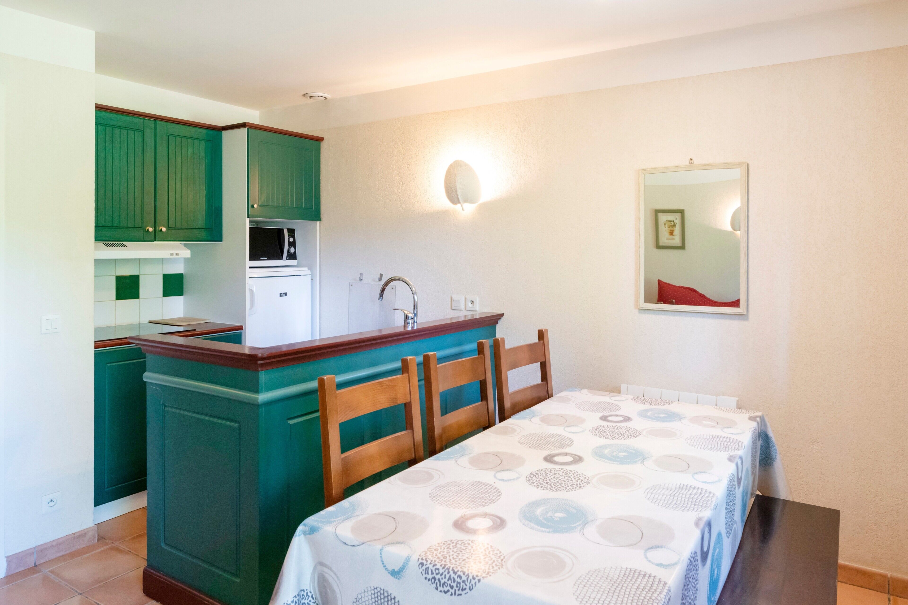 A compact kitchen with green cabinets, a white refrigerator, and a dining area with a table and chairs.