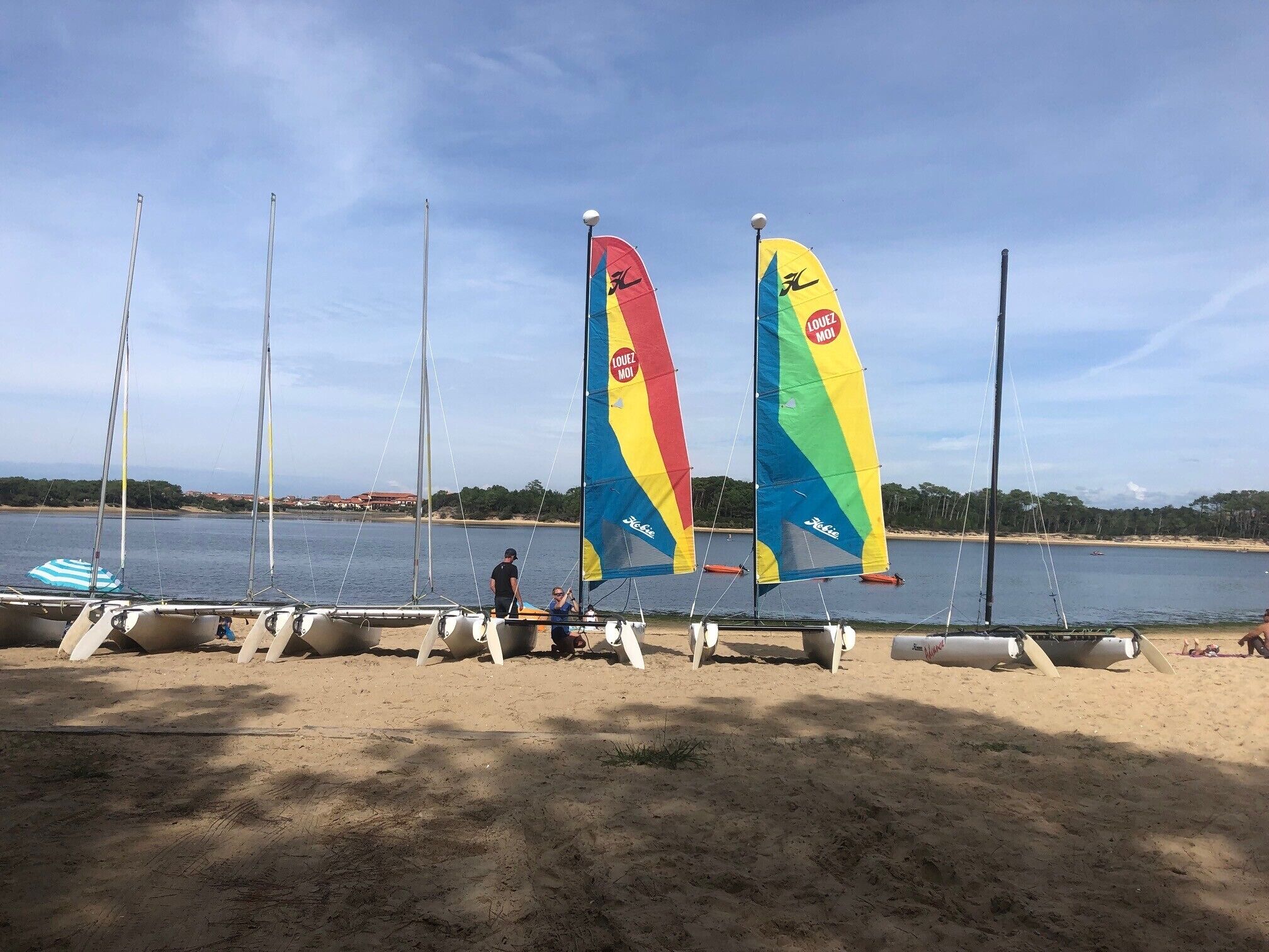 A beach with sailboats docked, a sandy shore, and a calm body of water in the background.