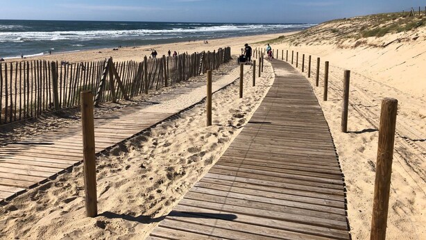 Una passerella di legno che conduce a una spiaggia sabbiosa, con le onde dell'oceano sullo sfondo.