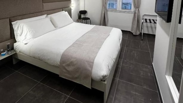 Una habitación de hotel moderna con una cama grande, una mesita de noche, un televisor y una ventana con cortinas.