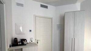 Una kitchenette pequeña con cafetera, un cesto de basura y un armario blanco.