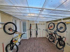 A covered outdoor area with a wooden floor, multiple bicycles mounted on walls, and a door leading to another room. - 'Joyfül Accomodation Camera P' with Wi-Fi and Air Conditioning (Finale Ligure)