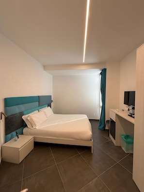 A modern bedroom with a bed, bedside table, desk, and a television. - 'Joyfül Accomodation Camera P' with Wi-Fi and Air Conditioning (Finale Ligure)