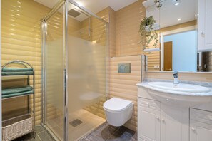 Un baño con cabina de ducha de vidrio, inodoro blanco, lavabo con encimera de mármol y espejo sobre el lavabo.