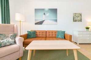 Une pièce comprenant un canapé, une table, une lampe, une commode et un tableau représentant un phare.